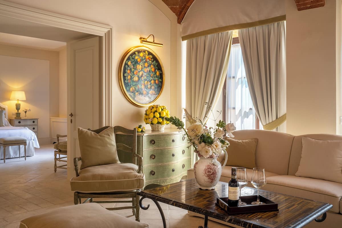 Un salon bien éclairé, avec un canapé, une table basse agrémentée d’un vase et de verres à vin, un tableau au mur et un lit à l’arrière-plan.