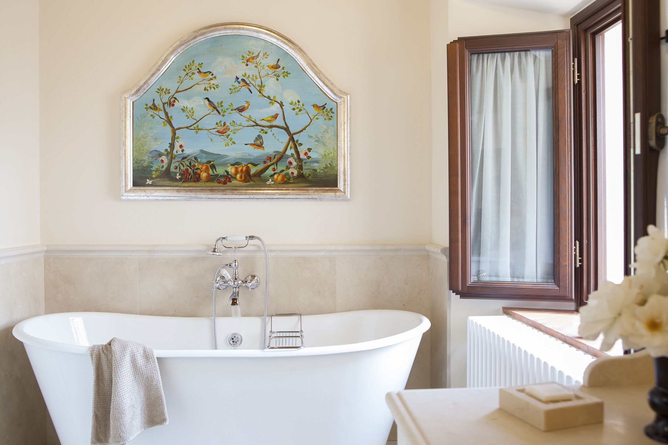 Ein Badezimmer mit einer freistehenden Badewanne, einem gerahmten Gemälde darüber und einem Fenster mit Vorhängen.