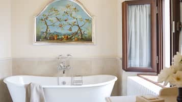 Ein Badezimmer mit einer freistehenden Badewanne, einem gerahmten Gemälde darüber und einem Fenster mit Vorhängen.