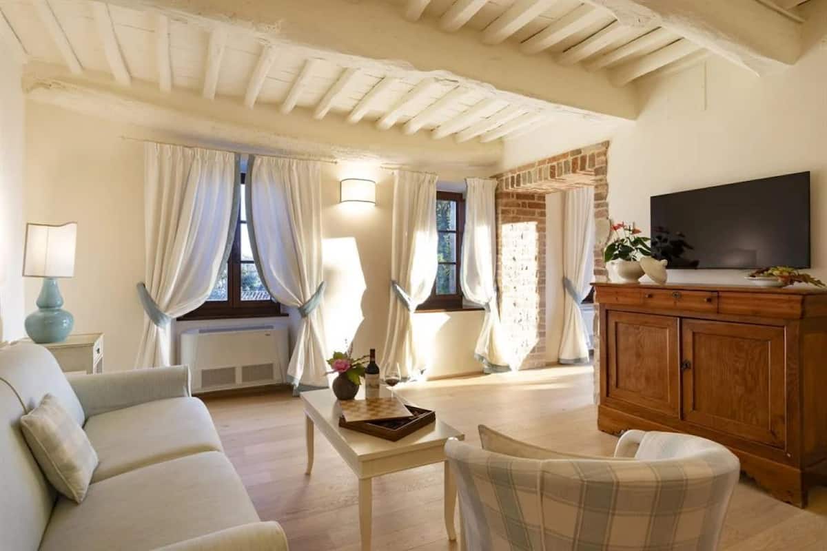 Un salon avec un canapé, une table sur laquelle se trouve une lampe, un téléviseur posé sur un meuble en bois et une fenêtre avec des rideaux.