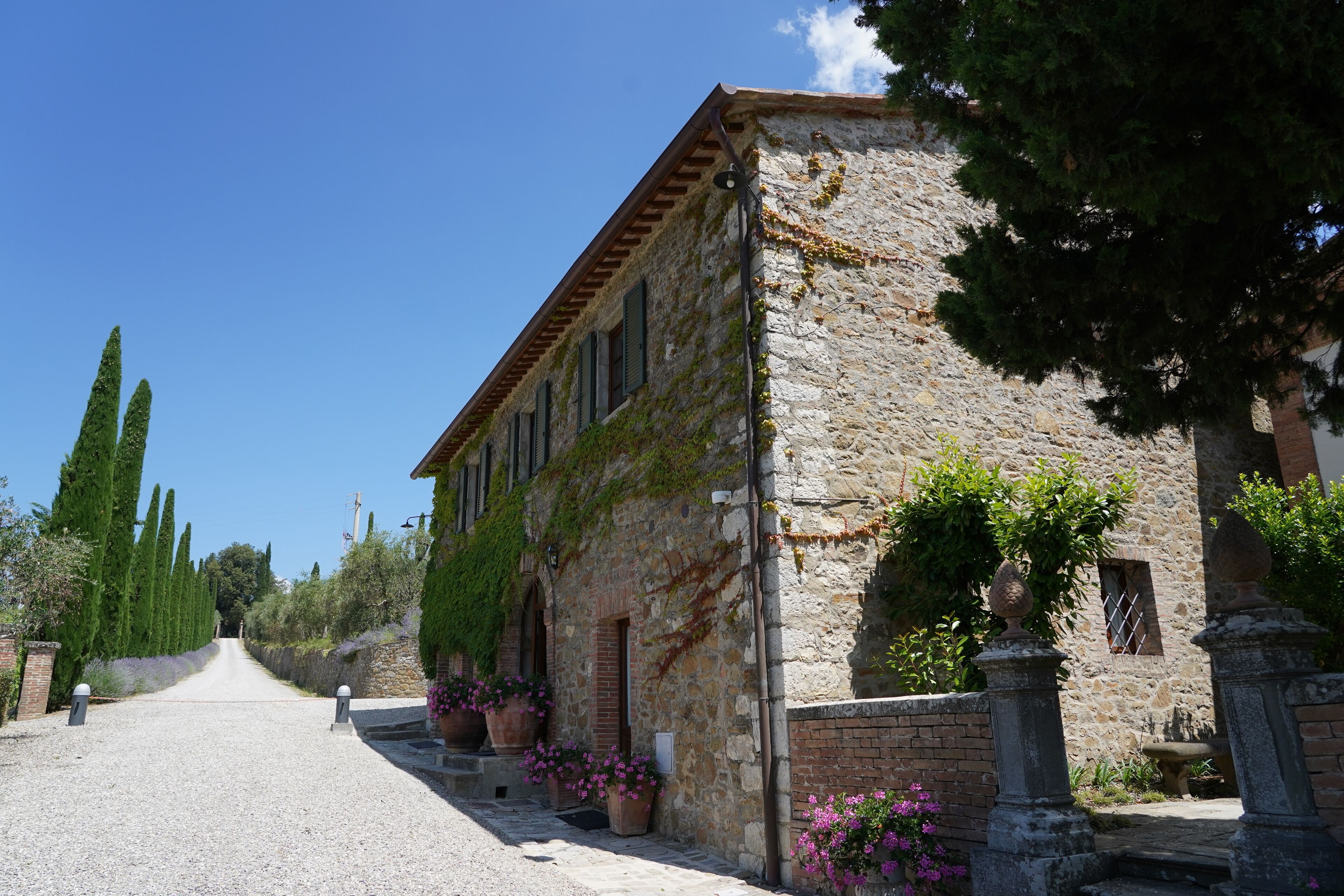 A stone building with a gravel driveway, potted plants, and a clear blue sky.