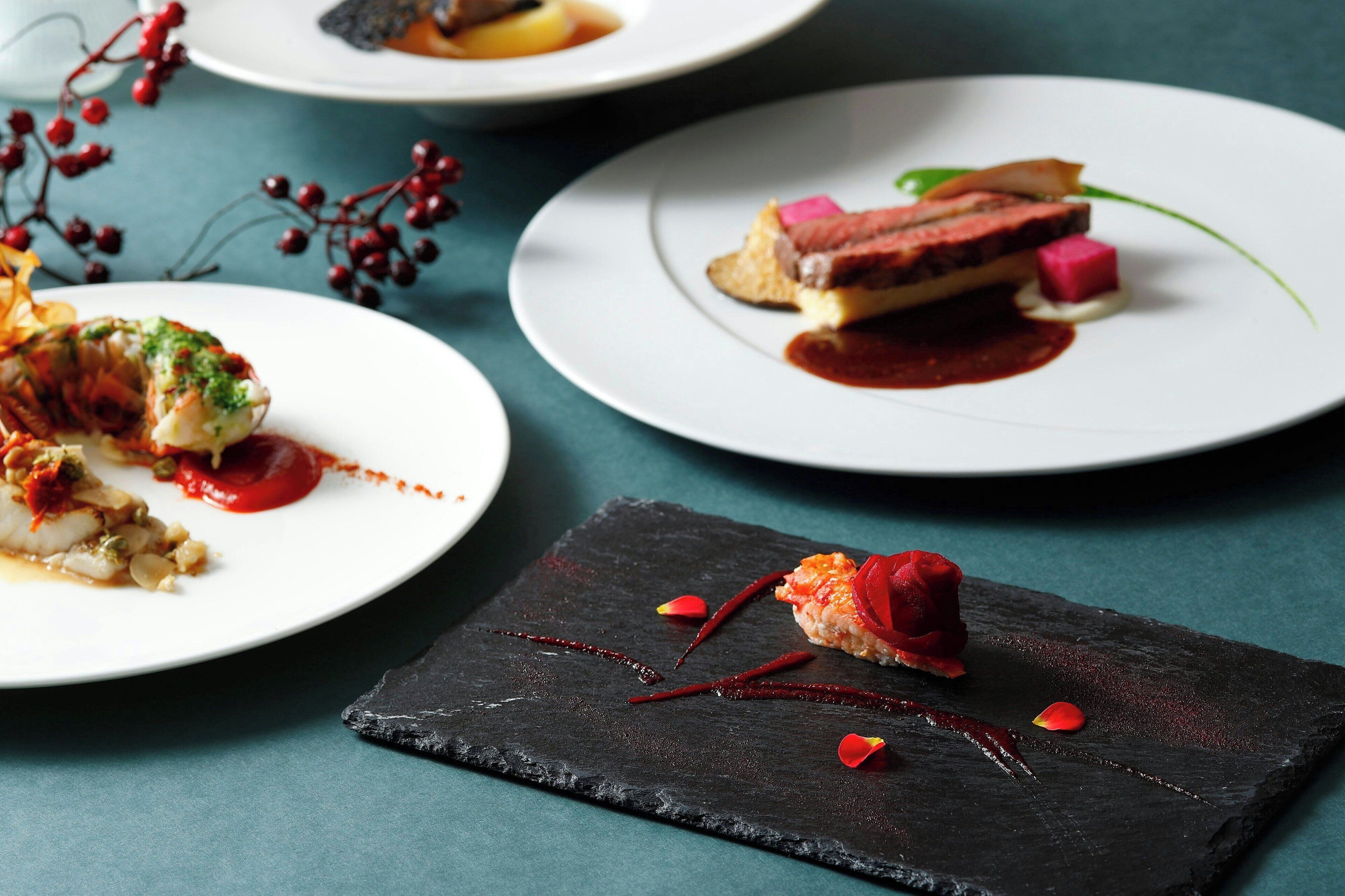 Three plates of gourmet dishes with a dark slate serving board in the foreground.