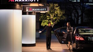 Un hombre y una mujer están de pie junto a un coche negro con un cartel de Marriott.