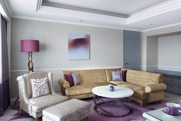 Una sala de estar moderna con un sofá color beige, un sillón a juego, una mesa de centro redonda y una lámpara de acento morada.