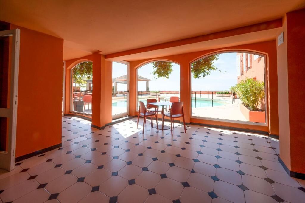 A room with a tiled floor, a table with chairs, and large windows offering a view of a pool and outdoor area.