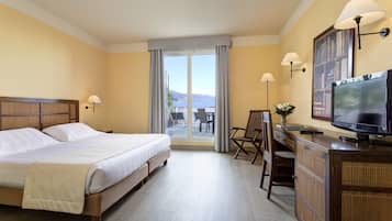 A hotel room with a large bed, a desk with a television, and a view of the outdoors through the window.