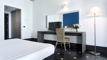 Habitación de hotel con cama, escritorio, computadora, silla, lámpara y espejo.