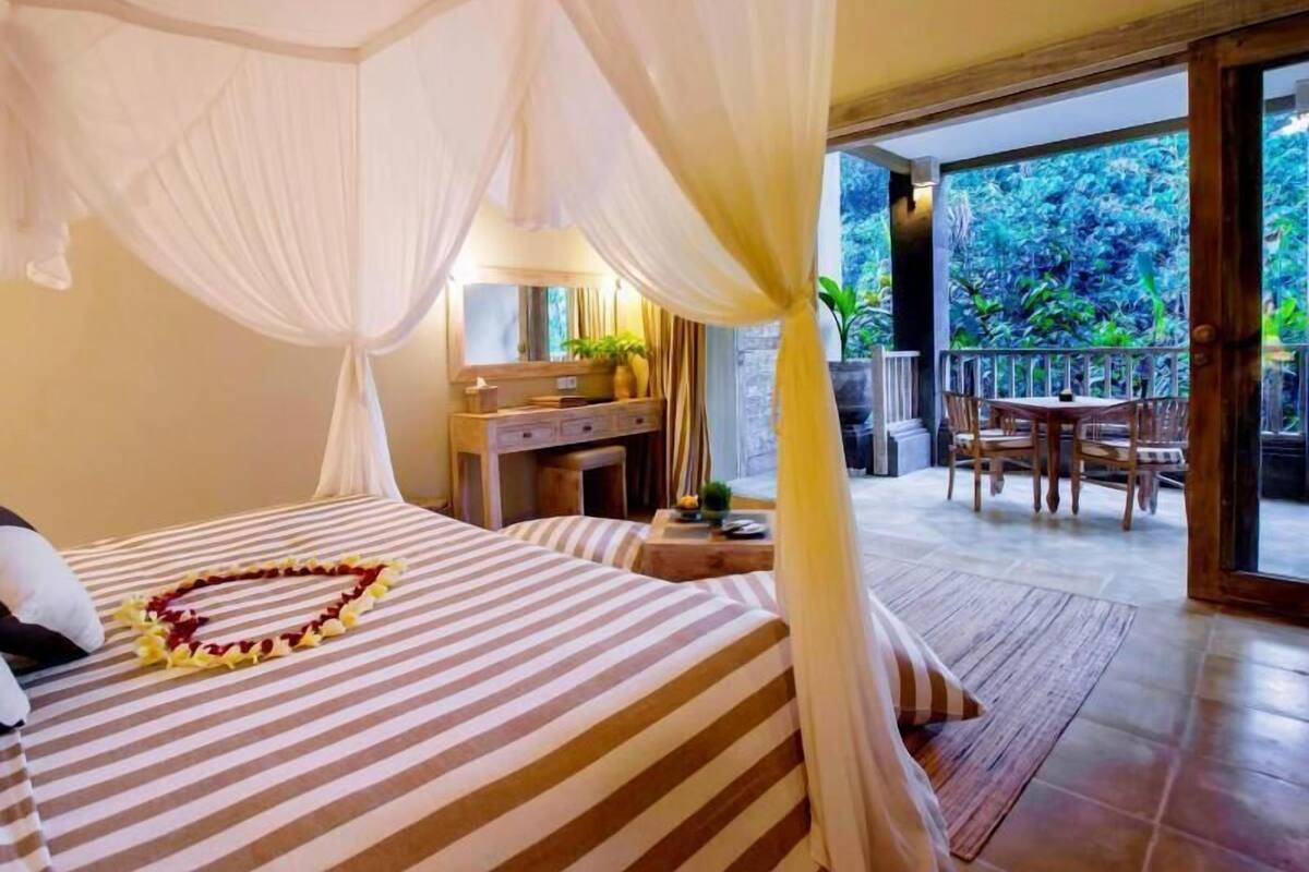 A room with a bed, a desk, and a balcony with a view of greenery.