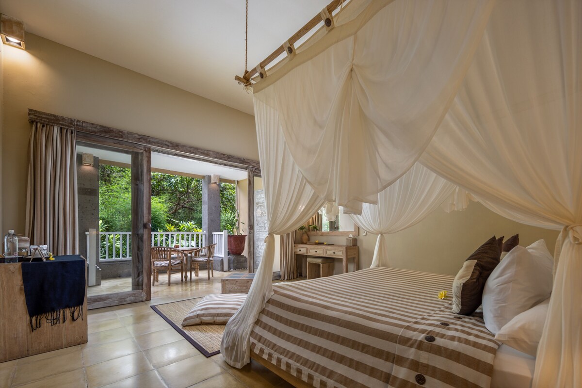 A bedroom with a canopy bed, a wooden desk, and a balcony with outdoor furniture.