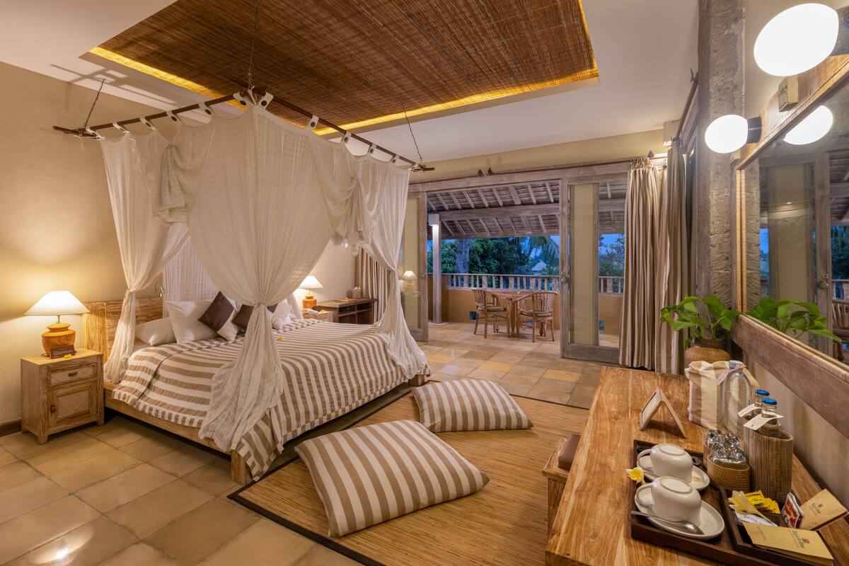 A bedroom with a canopy bed, a wooden bedside table, a nightstand, and a breakfast tray with cups and a bottle.