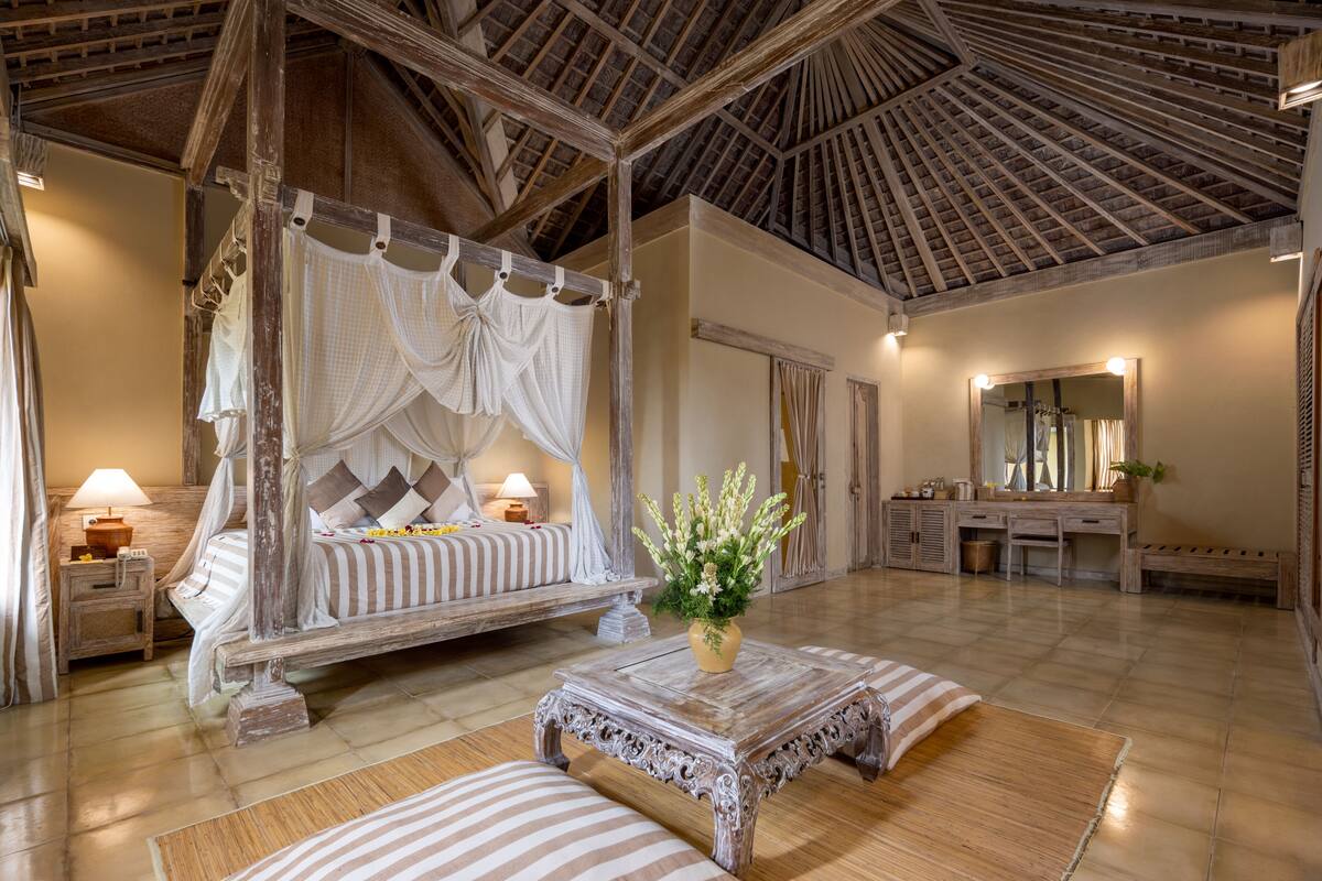 A four-poster bed with a canopy, a wooden coffee table, a mirror, and a vanity with a sink.