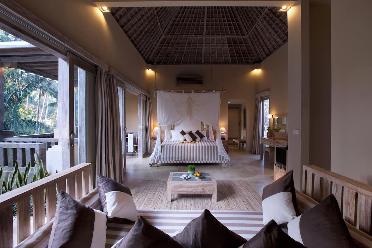 A bedroom with a canopy bed, a wooden coffee table, and a view of the outdoors.