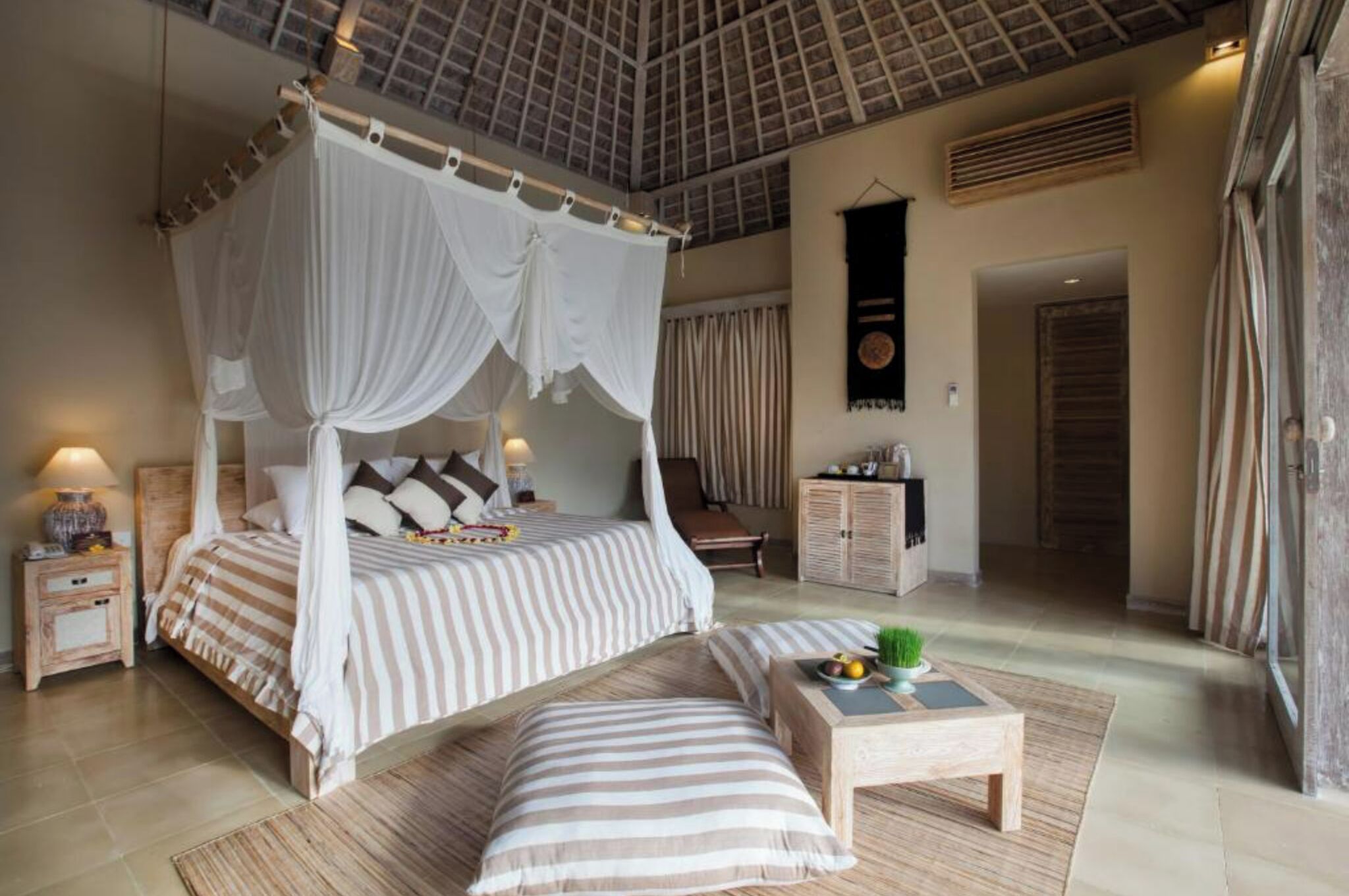 A bedroom with a four-poster bed, a bedside table with a lamp, a small table with fruit, and a view of the room.