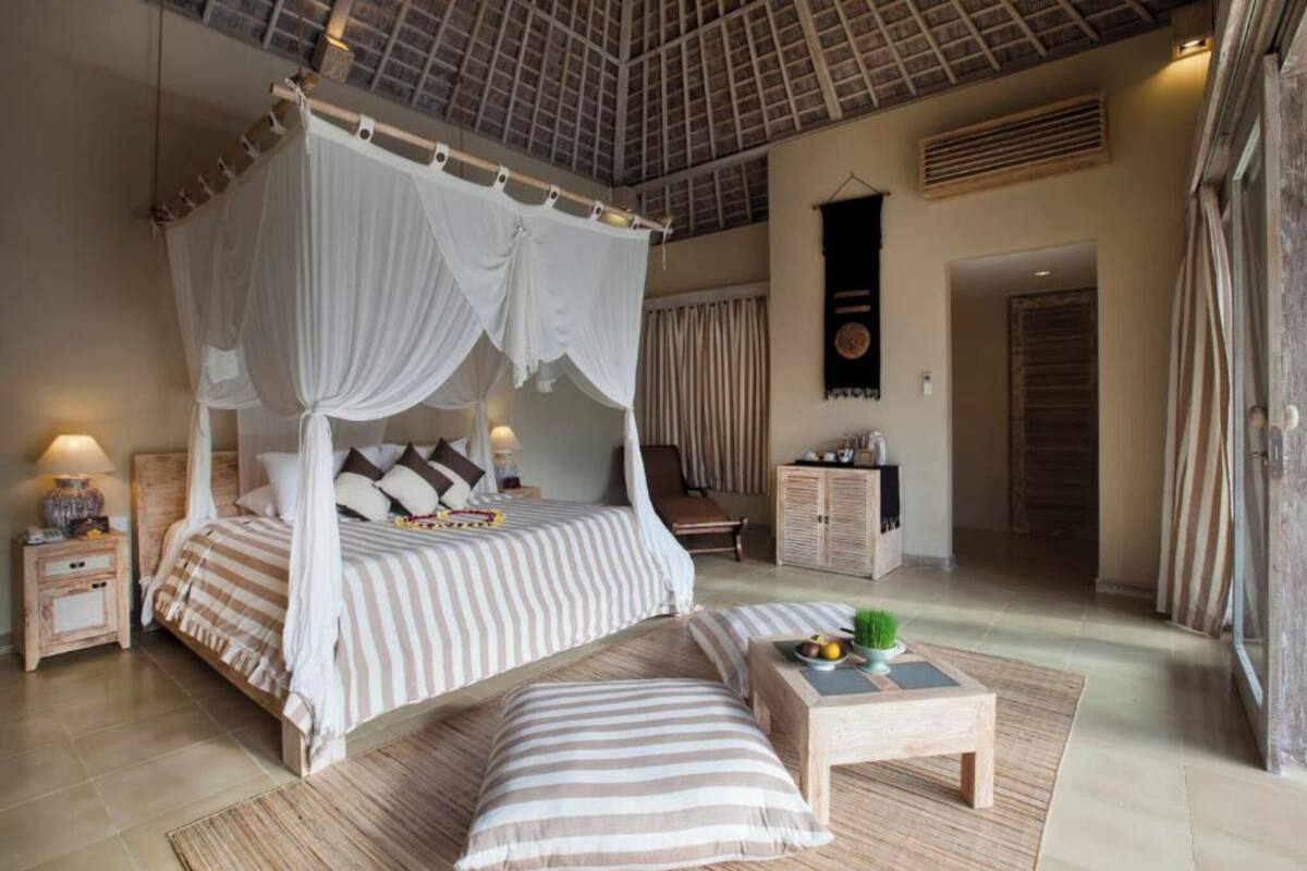 A bedroom with a four-poster bed, a bedside table with a lamp, a small table with fruit, and a view of the room.