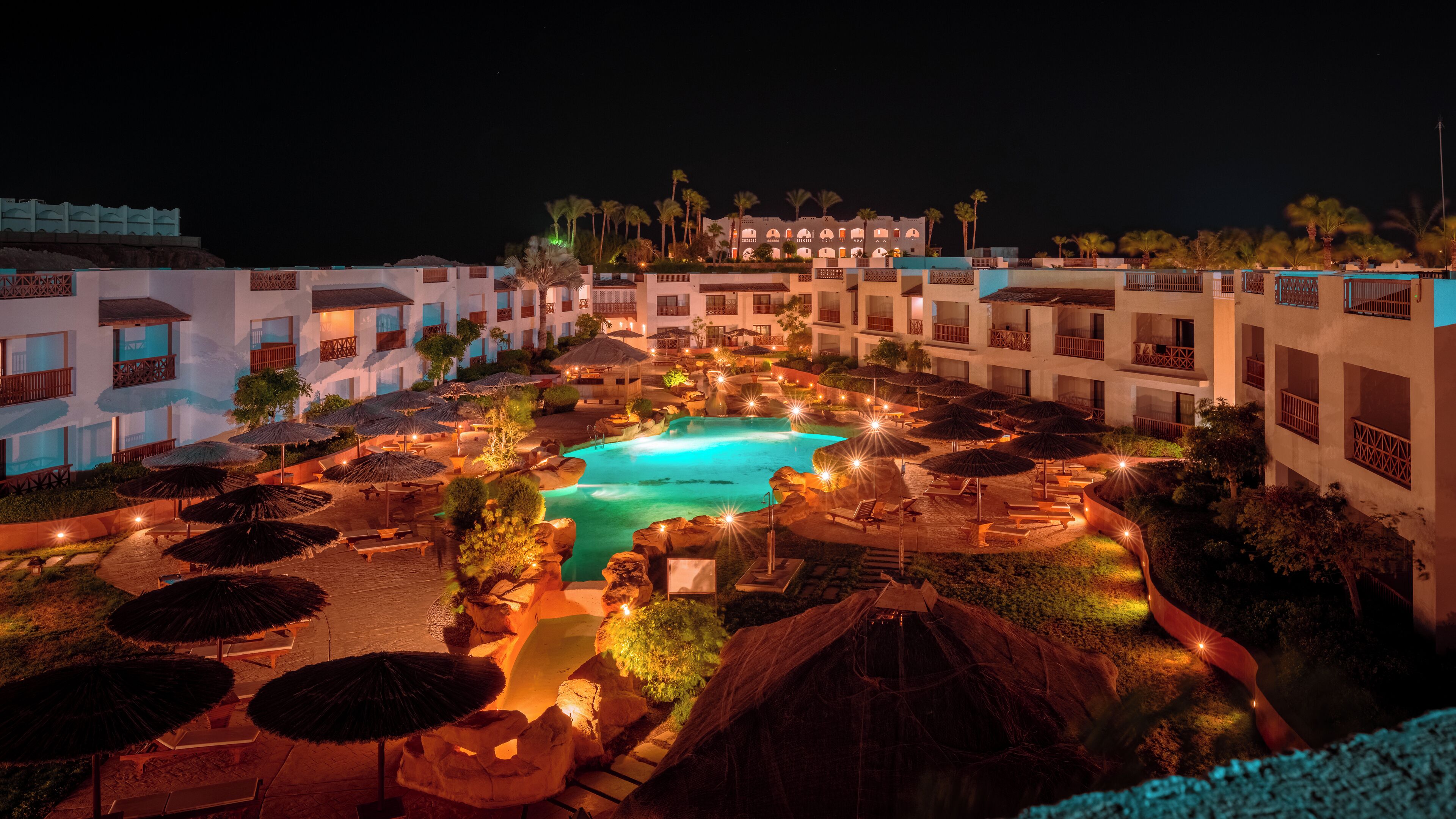 Un resort con piscina central, varios balcones y zonas de estar al aire libre.
