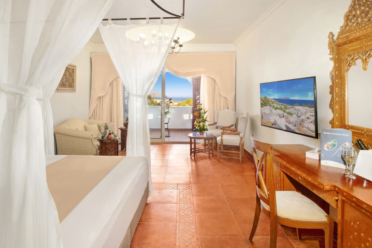 Une chambre d’hôtel comprenant un lit, un coin salon avec une table et des chaises, un balcon avec vue et un tableau au mur.