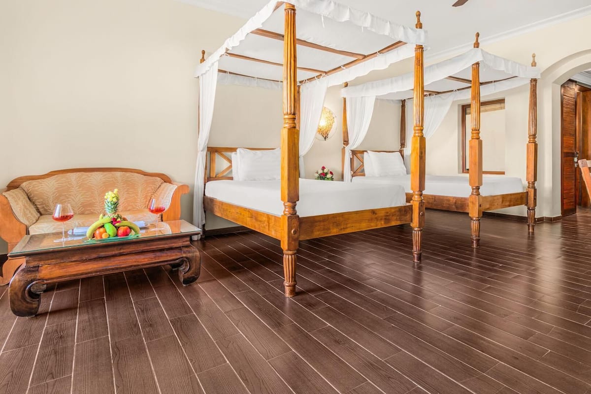 A four-poster canopy bed with a wooden frame, a sofa with a glass coffee table, and a wooden chair.