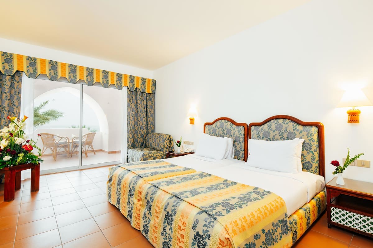 Une chambre d’hôtel avec un grand lit, une chaise, une petite table, une table de chevet et une vue sur l’extérieur.