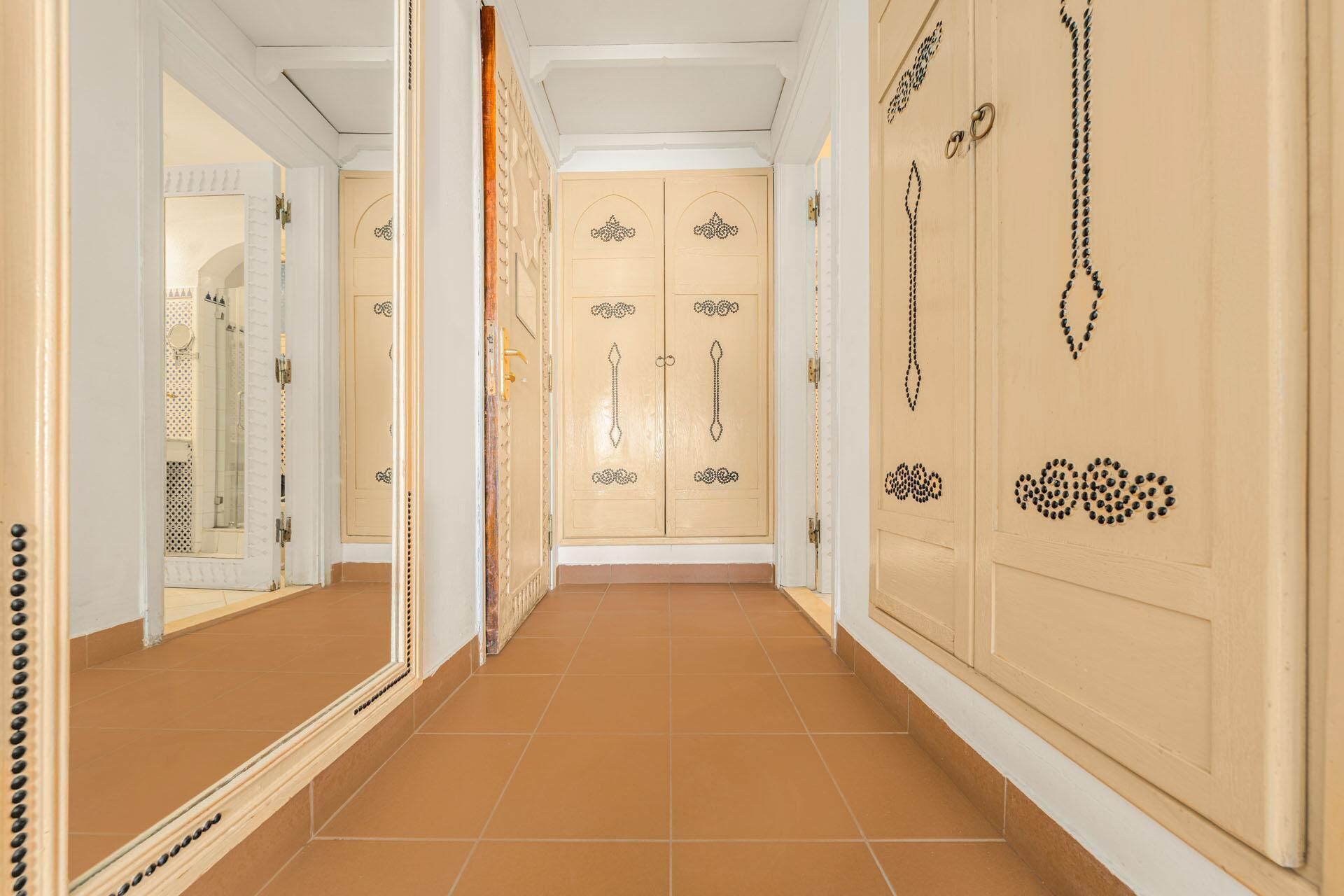 A hallway with beige doors, a mirror, and a tiled floor.