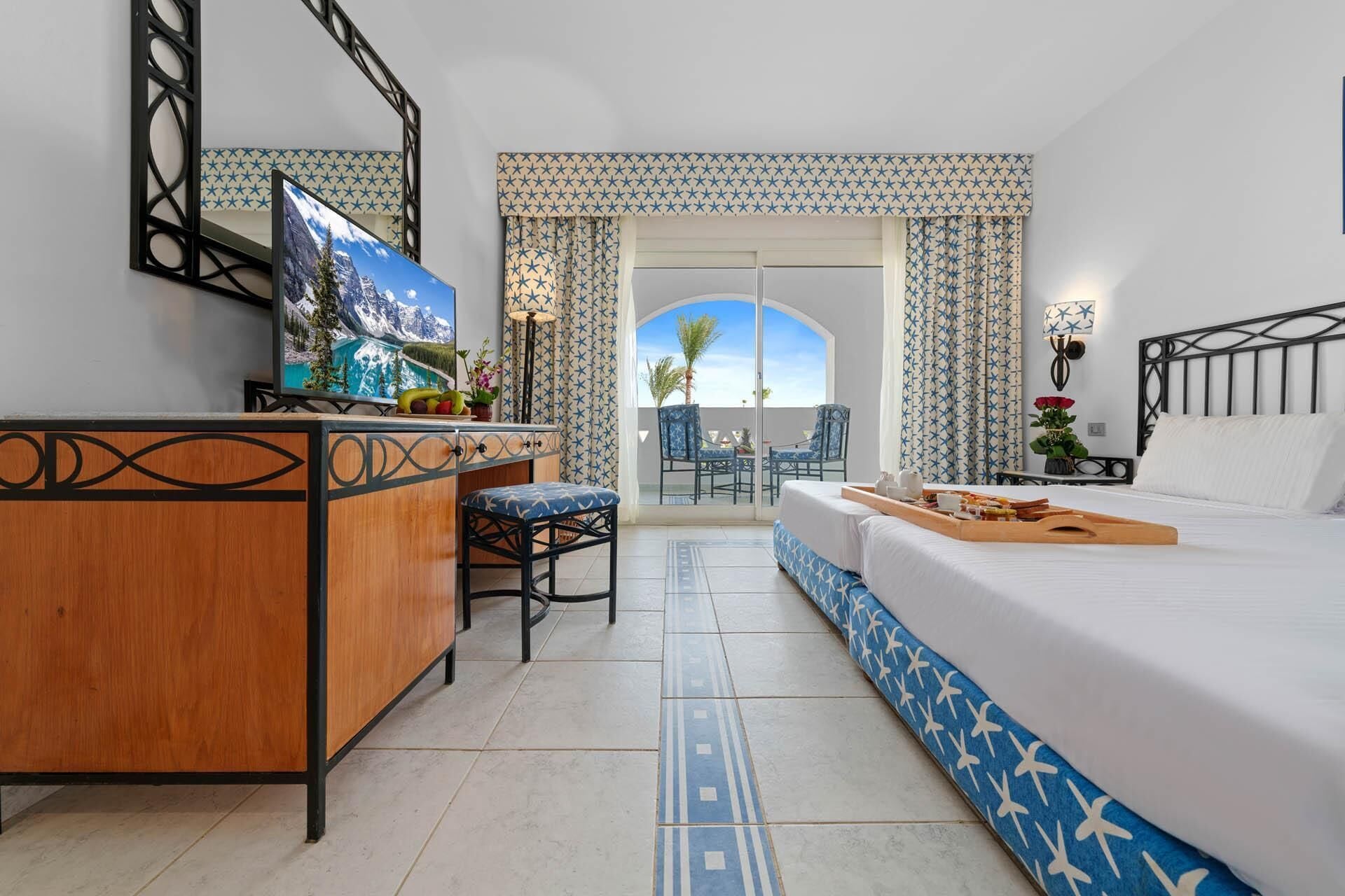 Una camera d'albergo con un letto, una scrivania, una televisione e un balcone con vista sulle montagne.