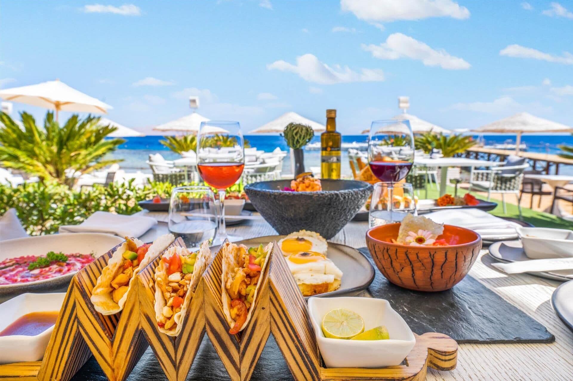 Un montaje para comer frente al mar, con diferentes platos, bebidas y vistas al océano.