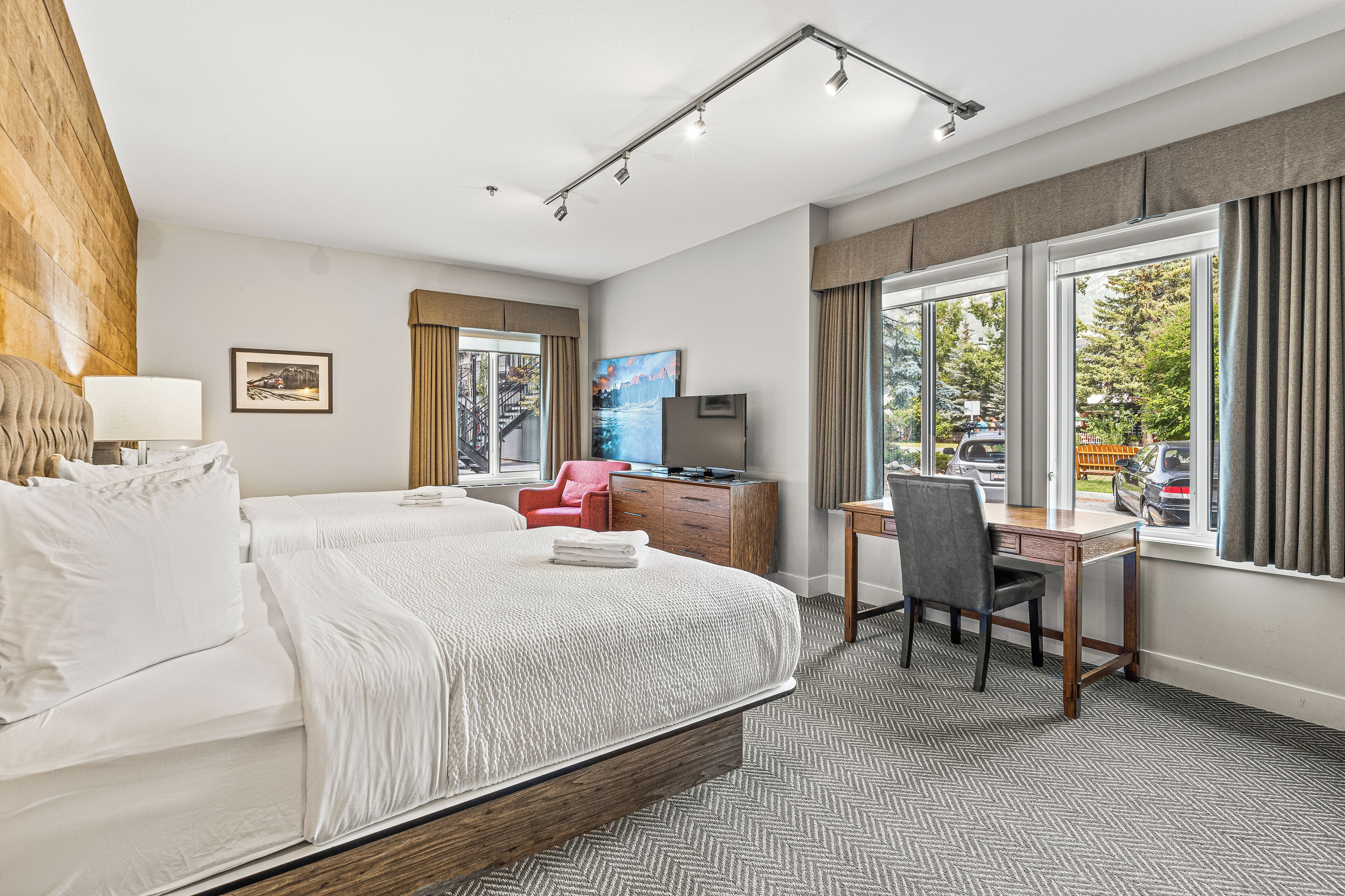 A hotel room with a large bed, a desk, a chair, a TV, and a window with a view of the outside.