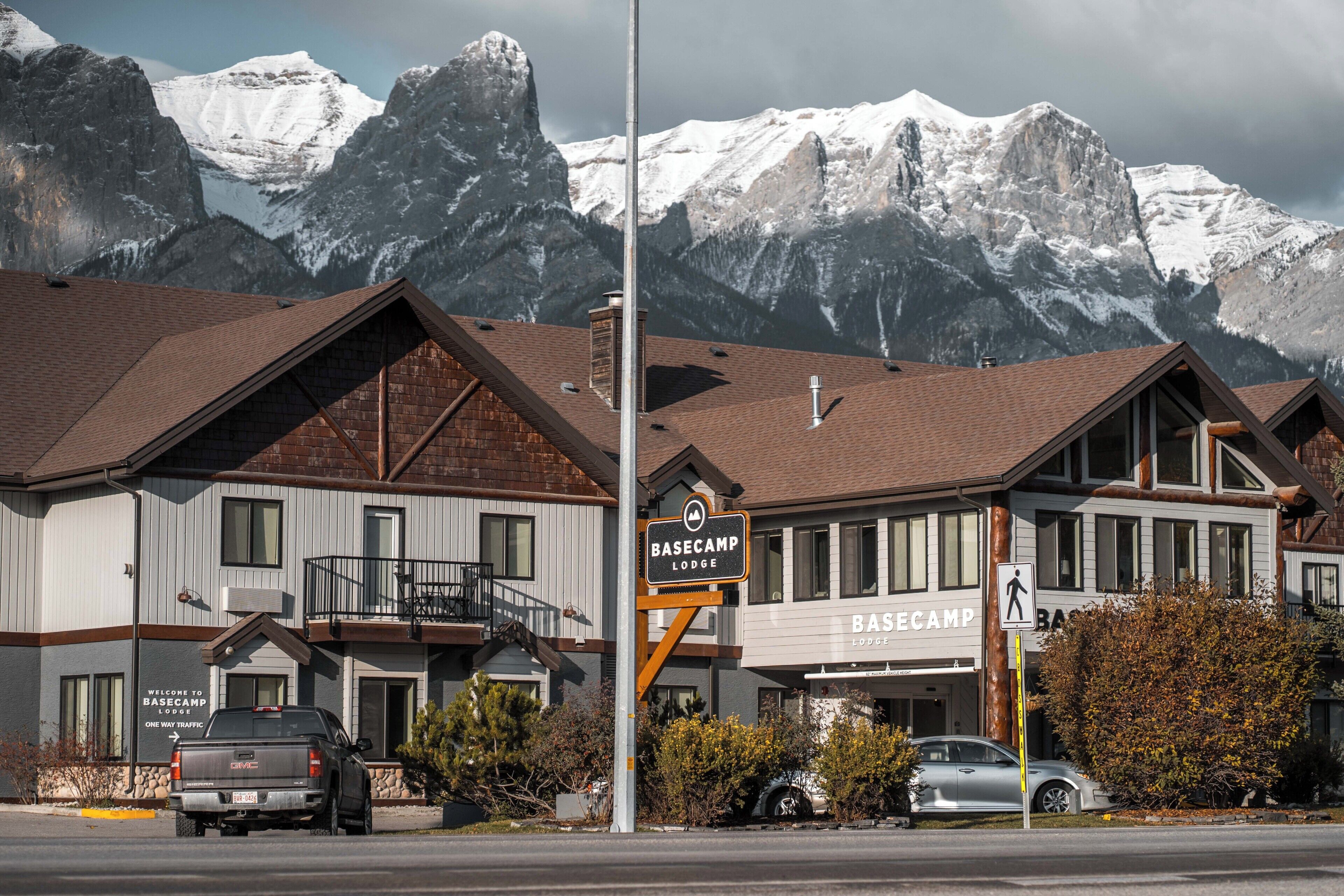 A lodge with a mountain backdrop, featuring a signboard, a vehicle, and a pedestrian sign.