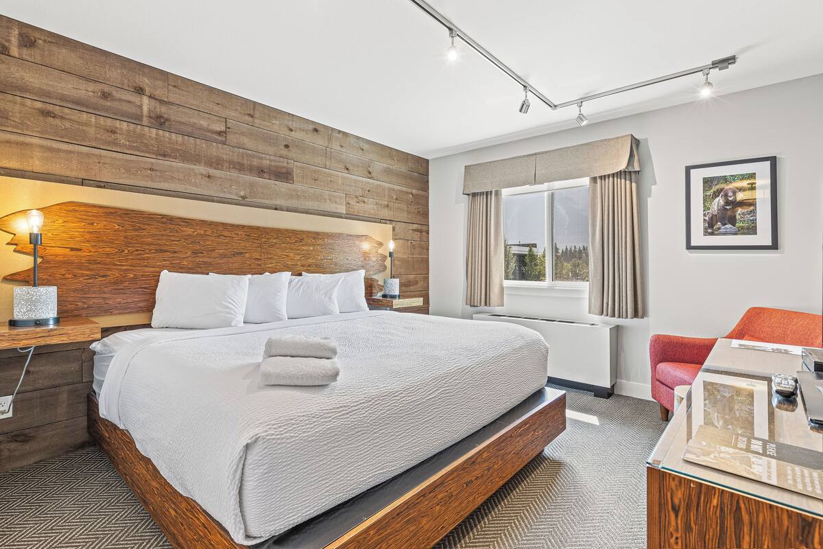 A modern hotel room with a large bed, wooden headboard, and a view of the outdoors through a window.