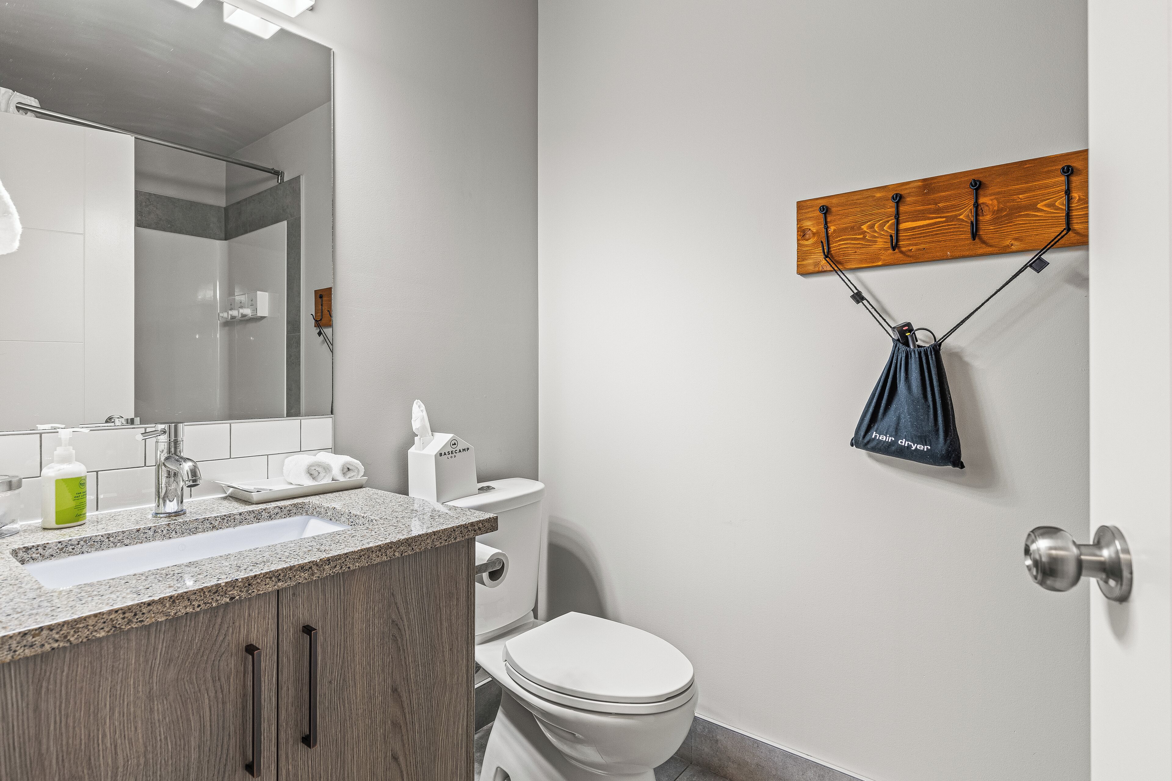 Une salle de bain moderne avec un lavabo à vasque en granit, un miroir, un meuble-lavabo en bois, des toilettes et un porte-serviettes muni d’un sèche-cheveux.