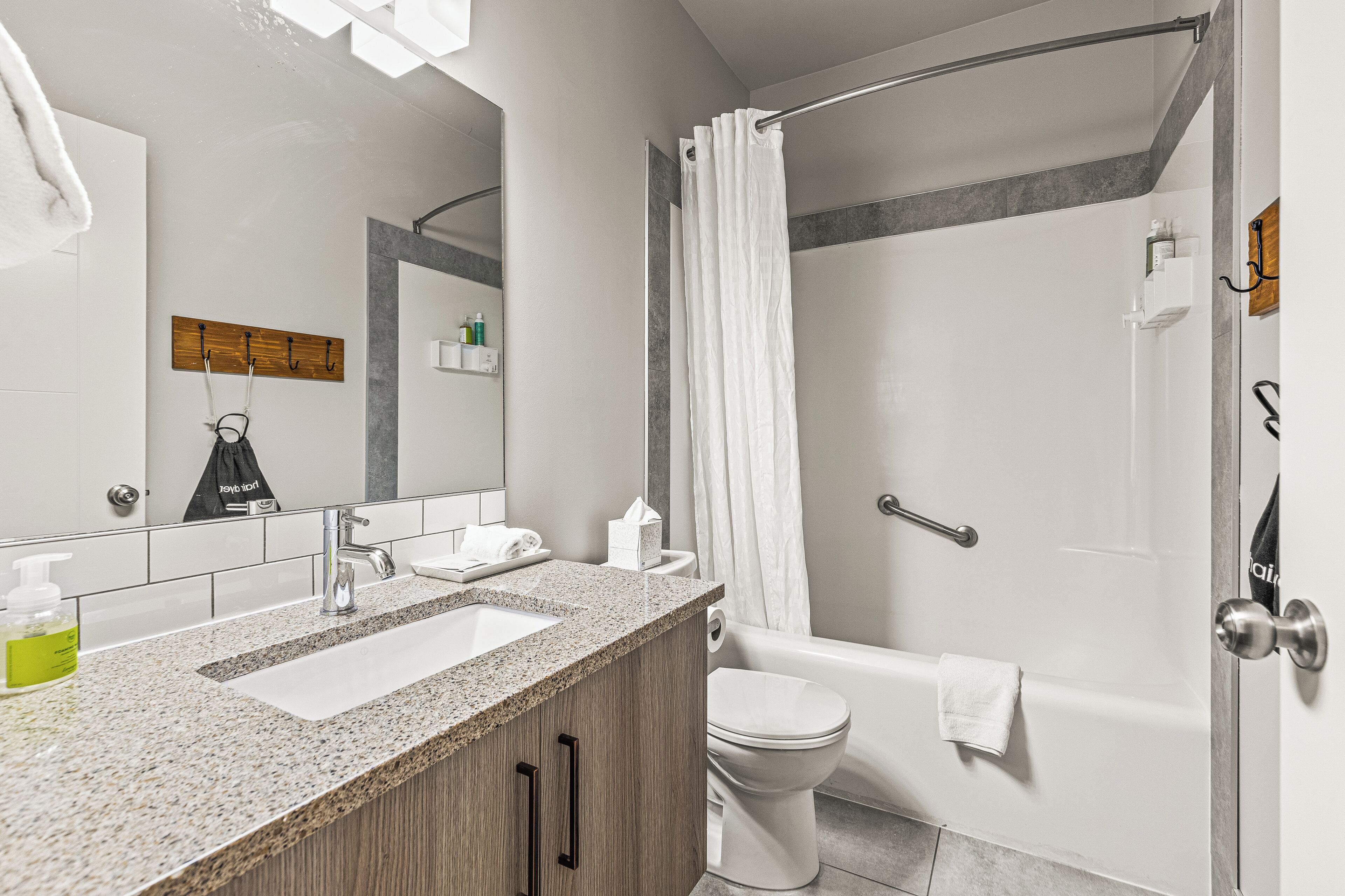A modern bathroom with a granite countertop sink, a toilet, and a shower with a curtain.