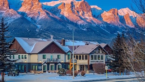 A lodge with a sign reading "BASE CAMP LODGE" in front of a mountain range. - Basecamp Lodge Canmore (Canmore)