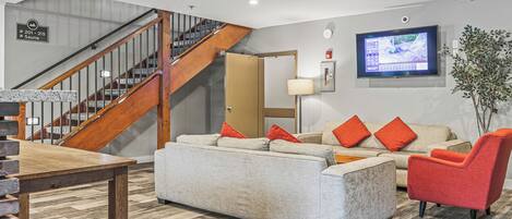 A modern hotel lobby with a staircase, a sofa set, a television, and a plant.