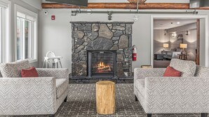 A cozy living area with a stone fireplace, two patterned sofas, a wooden coffee table, and a view into a dining area. - Basecamp Lodge Canmore (Canmore)