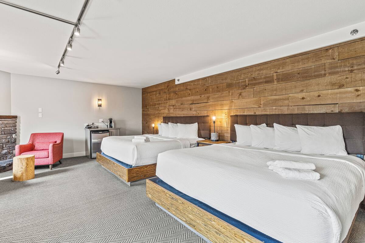 A hotel room with two beds, a red chair, a small table, and a wooden accent wall.