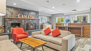 A cozy living area with a stone fireplace, a sofa with red cushions, a wooden coffee table, and a reception desk with a computer. - Basecamp Lodge Canmore (Canmore)