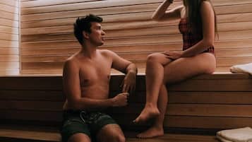 Two people sitting on wooden benches in a sauna room with slatted wooden walls.