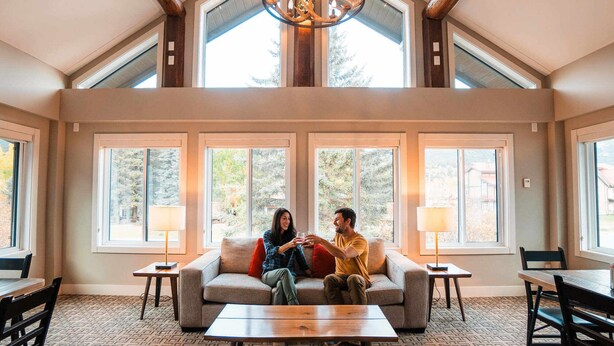 A spacious living room with a high ceiling, large windows, and a chandelier. - Basecamp Lodge Canmore (Canmore)