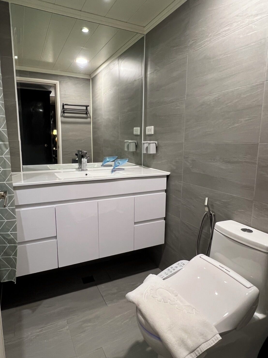 A modern bathroom with a large mirror, white vanity, and a toilet.