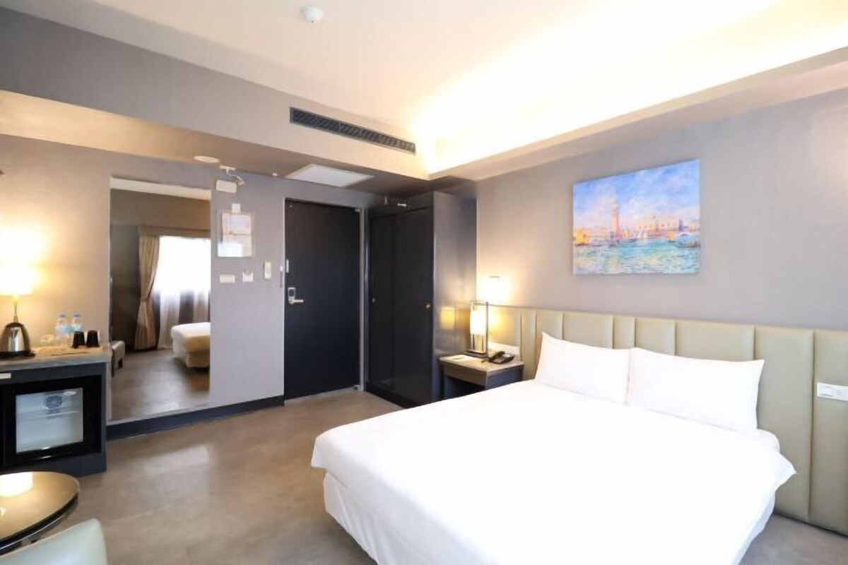 Una habitación de hotel con una cama grande, mesitas de noche, un escritorio y un cuadro en la pared.