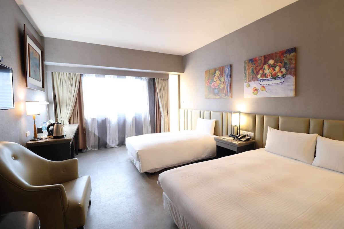 Habitación de hotel con dos camas, un escritorio, una silla, un televisor y una ventana con cortinas.