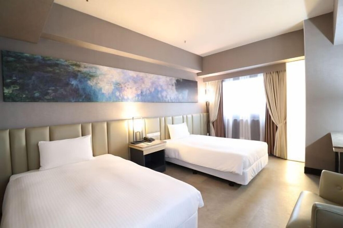 Habitación de hotel con dos camas, un cuadro abstracto grande en la pared, un escritorio y vistas al exterior a través de la ventana.