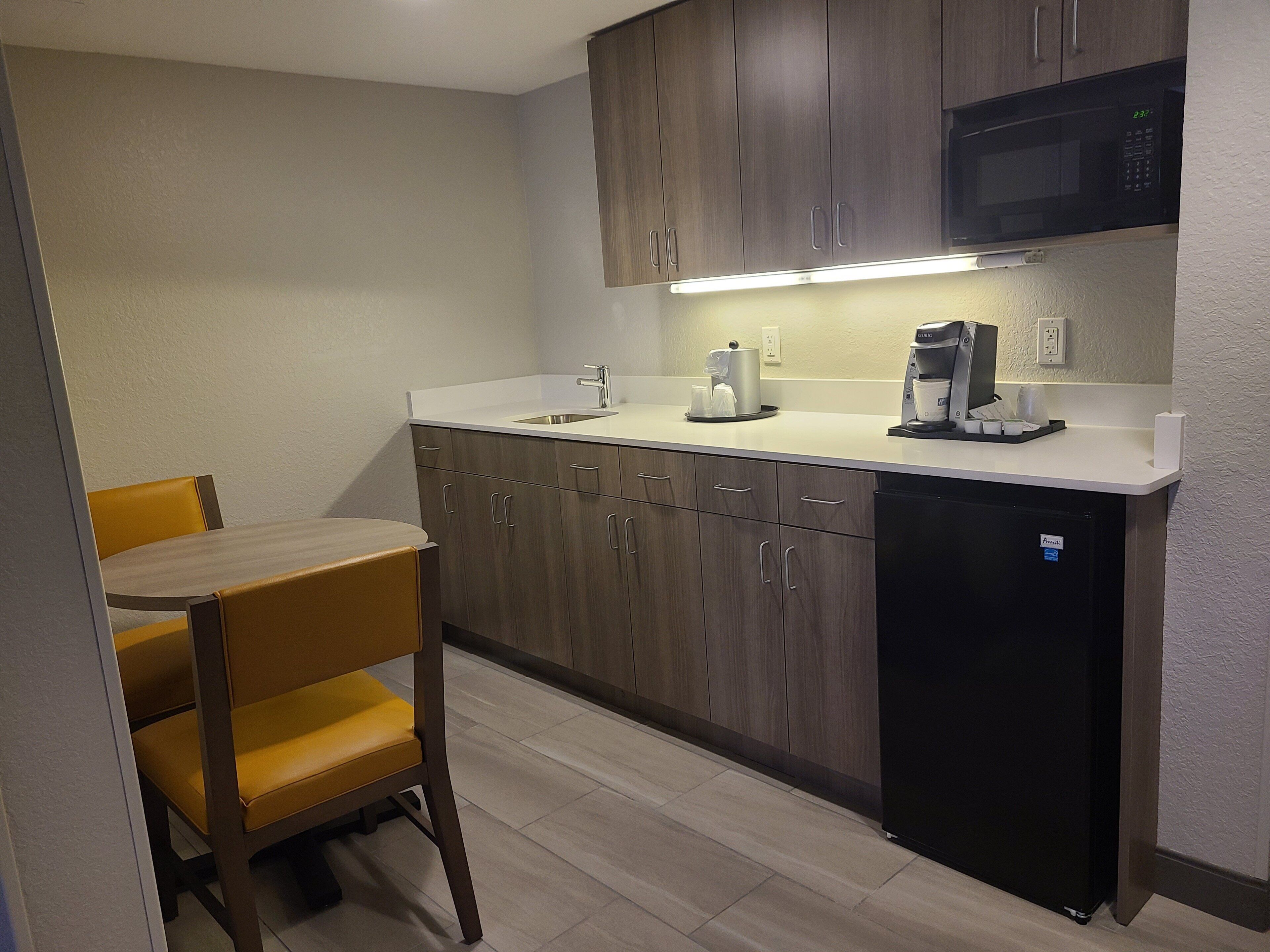 A compact kitchen with wooden cabinets, a built-in microwave, a coffee maker, and a sink.