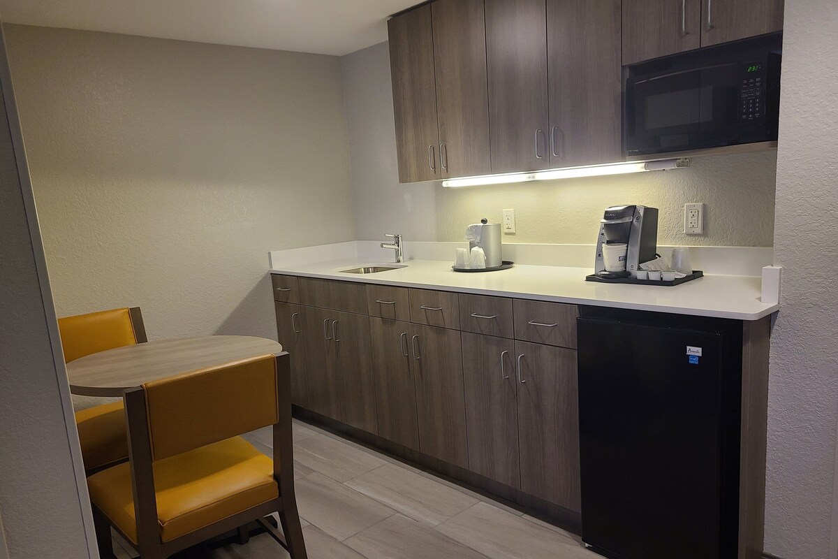 Cocina compacta con armarios de madera, un lavamanos, microondas y cafetera.