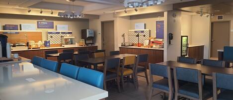 A modern breakfast area with a central counter, seating, and various food service stations.