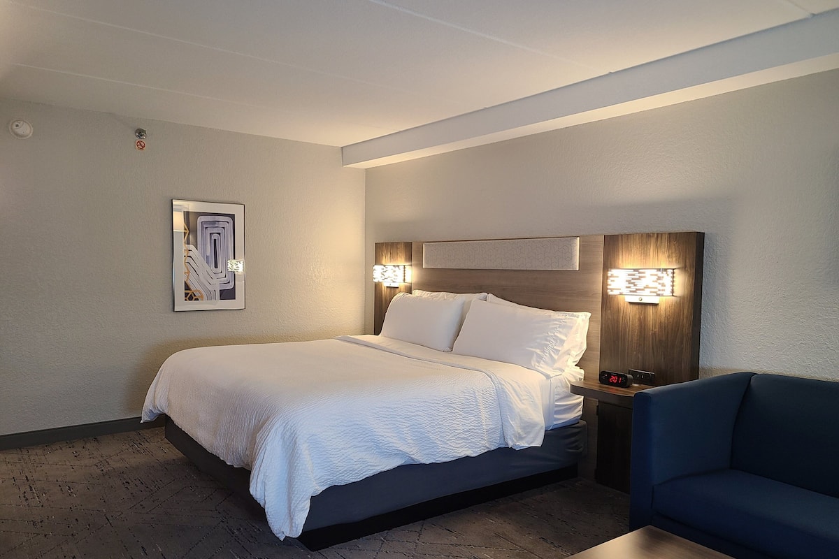 Ein Hotelzimmer mit einem Bett, Nachttischen, einem blauen Sofa und einer Wanduhr.