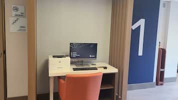 Een kleine kantoorruimte met een bureau, stoel en computerscherm. Een bord op de muur geeft aan dat roken verboden is en dat de trapdeur gesloten moet blijven.