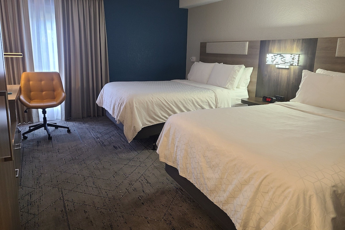 Habitación de hotel con dos camas, un escritorio y una silla.