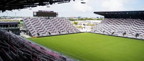 A stadium with multiple tiers of seating, a large green field, and a scoreboard.