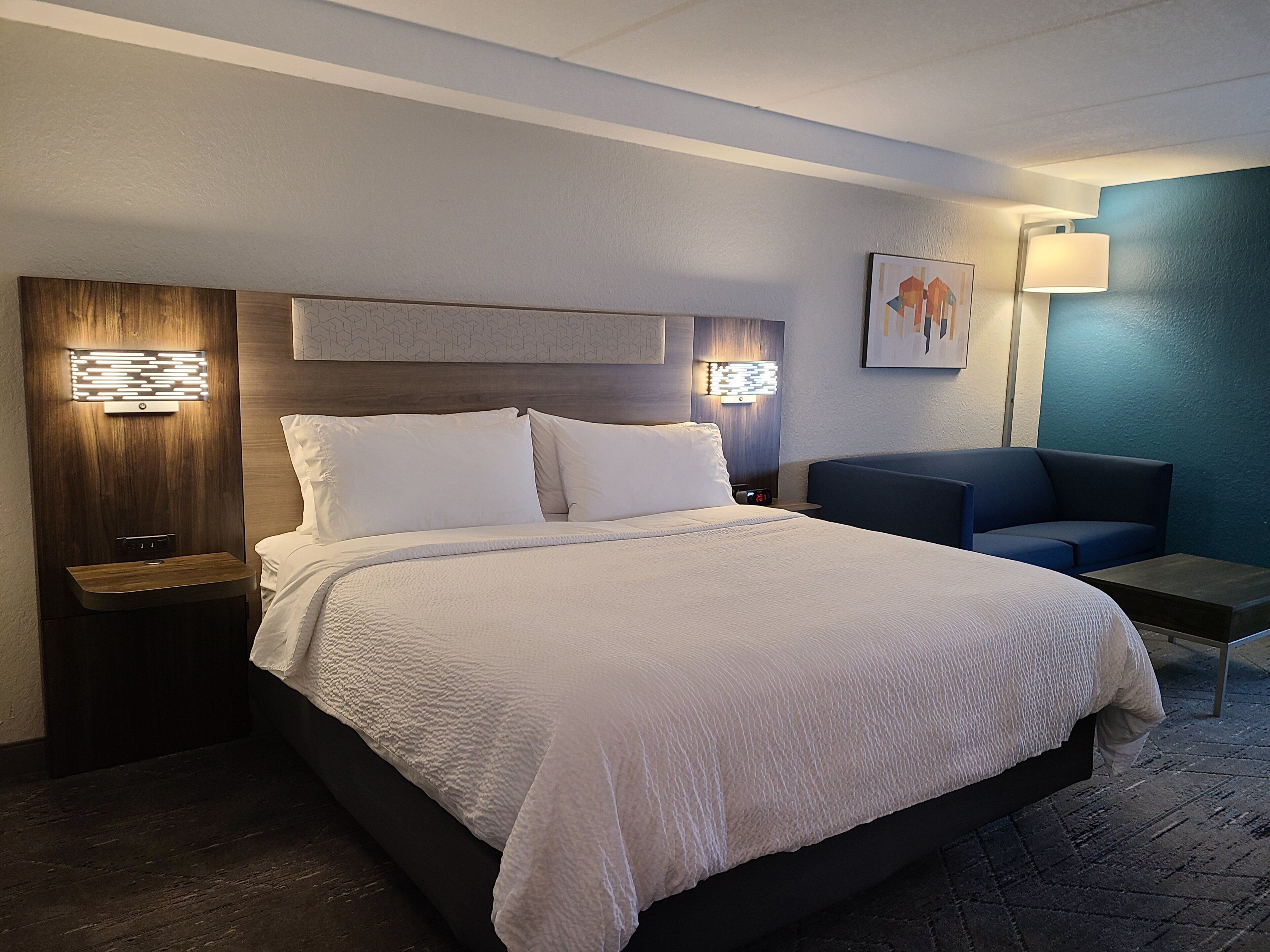 A hotel room with a large bed, bedside tables, a nightstand, a seating area, and a wall-mounted lamp.