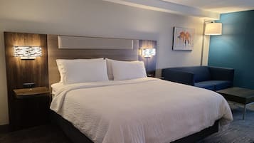 A hotel room with a large bed, bedside tables, a nightstand, a seating area, and a wall-mounted lamp.